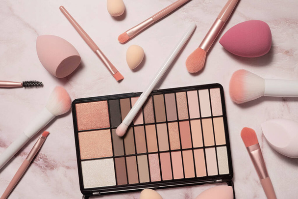 A nude eyeshadow palette and makeup artist's tools on a marble vanity. Brushes for powder, blush, eyebrows, shadows and sponges for concealer and foundation. - Fotografie, Obrázek