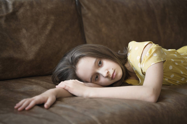 frustrated thoughtful teen girl lies on the brown couch - Фото, зображення