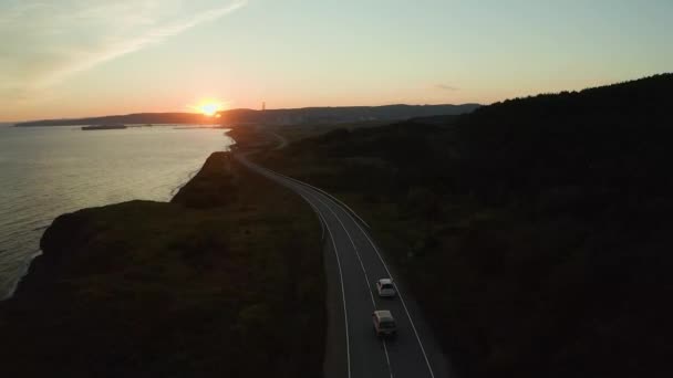 A family car drives in the evening at sunset in the summer along the highway next to the seashore enjoying a beautiful sunset. A beautiful evening sunset along the seashore, the car drives along the road, view from the top. - Footage, Video