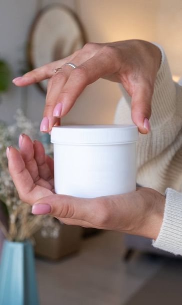 A woman opens a jar of hand cream - Фото, изображение