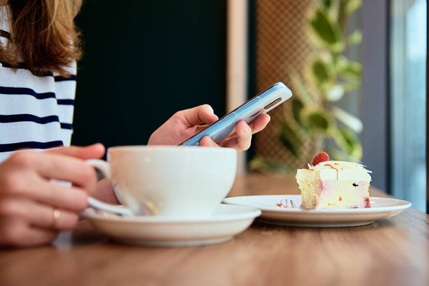 Γυναίκα χέρι χρήση smartphone στο καφέ, surfing πρόγραμμα περιήγησης στο internet, έχουν ένα διάλειμμα για καφέ. Ηλεκτρονική επικοινωνία και μέσα κοινωνικής δικτύωσης - Φωτογραφία, εικόνα