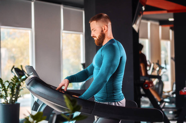 Portrait of a young bearded athletic man training on a treadmill. Concept of International Day of Sport. - Foto, Imagem