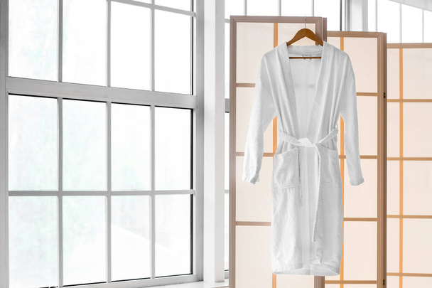 Розкладний екран з халатом біля вікна у світлій ванній кімнаті
 - Фото, зображення