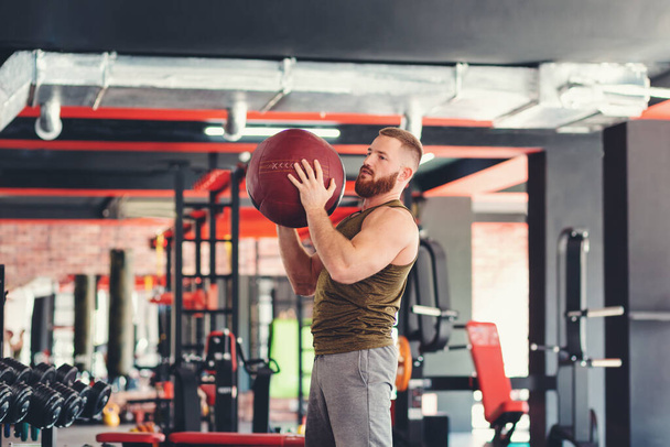 Portrait of a young bearded athletic man training in the gym with a sports med ball. Top view. Close-up. The concept of fitness - Photo, Image