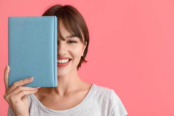 Beautiful young woman with book on pink background - Foto, immagini