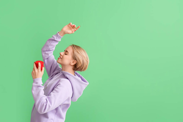 Женщина держит современный беспроводной портативный динамик на зеленом фоне - Фото, изображение