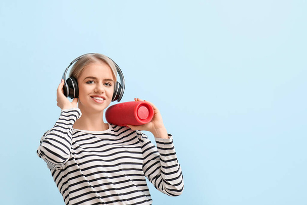 Woman with headphones holding modern wireless portable speaker on blue background - 写真・画像