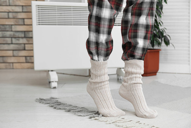 Woman in warm knitted socks near electric heater at home. Concept of heating season - Photo, Image