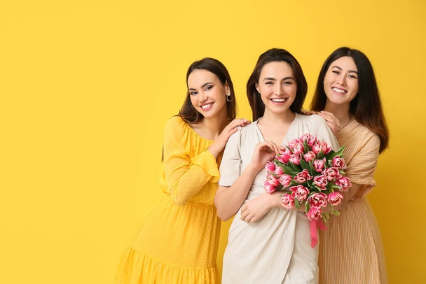 Beautiful women with bouquet of flowers on yellow background. International Women's Day celebration - Photo, Image