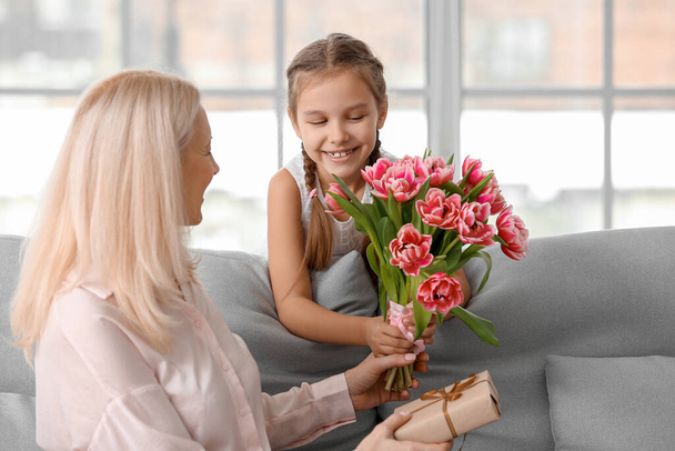 Niña saludando a su abuela con tulipanes en casa el Día Internacional de la Mujer - Foto, Imagen