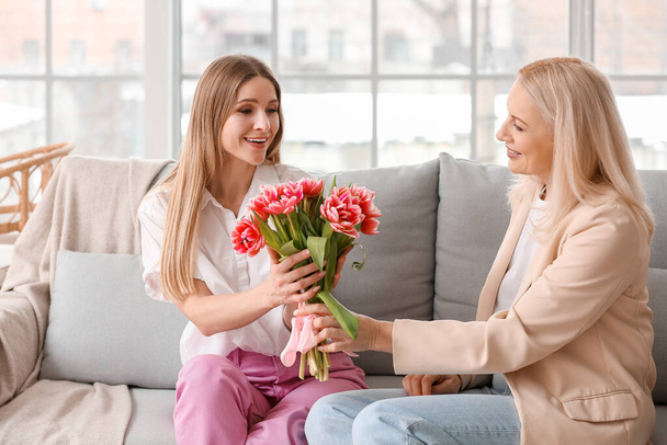 Young woman greeting her mother with bouquet of tulips at home on holiday - Foto, immagini