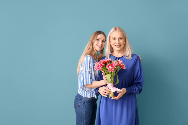 Young woman with her mother and bouquet of tulips on blue background - Photo, Image