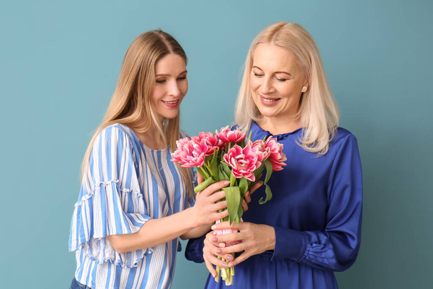 Junge Frau mit ihrer Mutter und einem Strauß Tulpen auf blauem Hintergrund - Foto, Bild