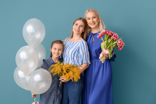 Young woman, her little daughter, mother with flowers and balloons on blue background - Photo, Image