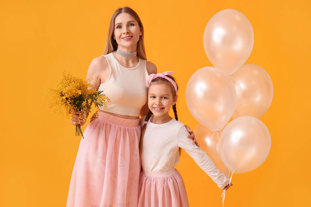 Niña, su madre con flores y globos sobre fondo amarillo - Foto, Imagen