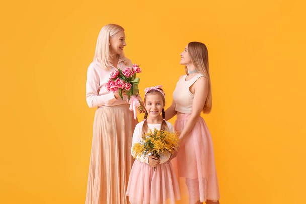 Young woman with her little daughter, mother and flowers on yellow background - Fotoğraf, Görsel
