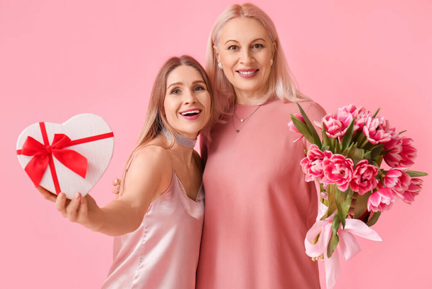 Young woman with her mother and gifts on pink background - Foto, imagen