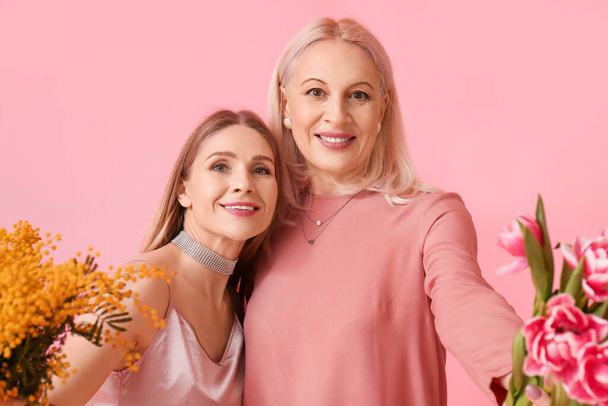 Young woman with her mother and flowers on pink background - Photo, Image