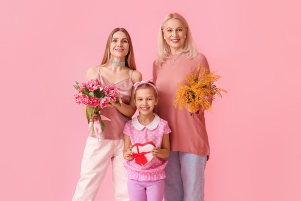 Young woman with her little daughter, mother and gifts on pink background - Photo, Image