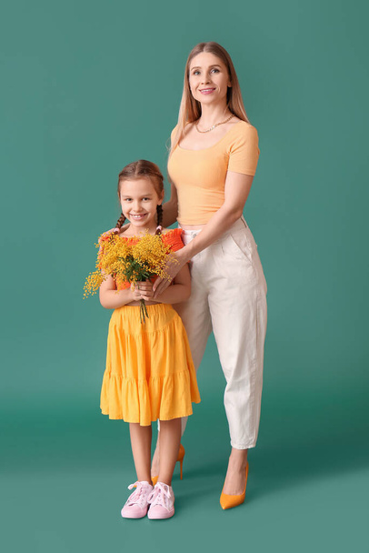 Little girl with mimosa flowers and mother on green background - Photo, Image