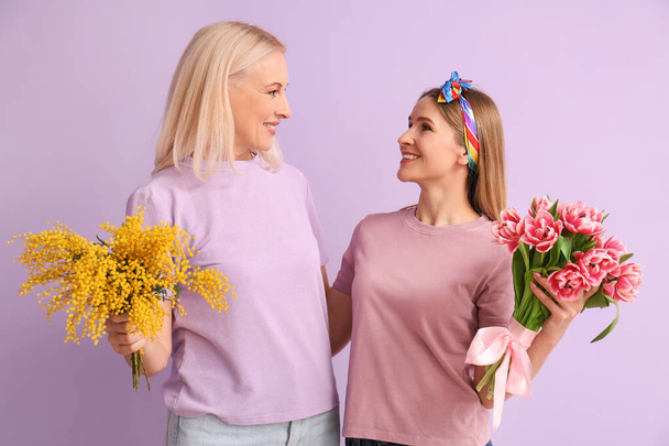 Young woman with her mother and flowers on lilac background - Photo, Image