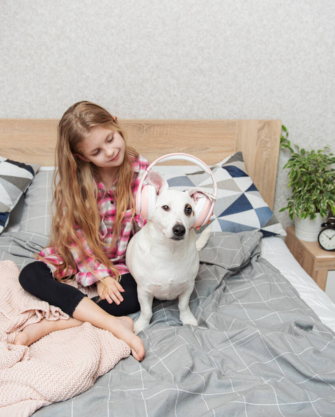 子供の娘と犬。小さな女の子置くヘッドフォンオン彼女の犬.   - 写真・画像