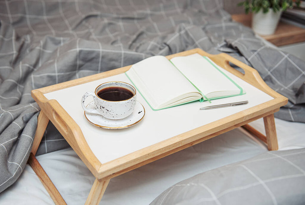 Breakfast in bed. Coffee and notebook on a wooden tray. Work at home concept. - Photo, Image