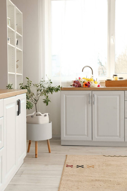 Stilvolle Kücheneinrichtung mit modernen Arbeitsplatten und Blumenstrauß in der Spüle - Foto, Bild