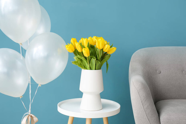 Armchair, tulips on table and air balloons near color wall - Photo, Image