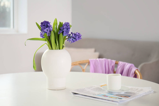 Sanomalehti, kuppi kahvia ja maljakko kukkia ruokapöydällä huoneessa - Valokuva, kuva