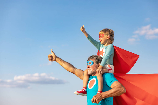 Superhero senior man and child playing outdoor. Super hero grandfather and boy having fun together against blue summer sky background. Family holiday concept. Happy Father's day - Fotó, kép