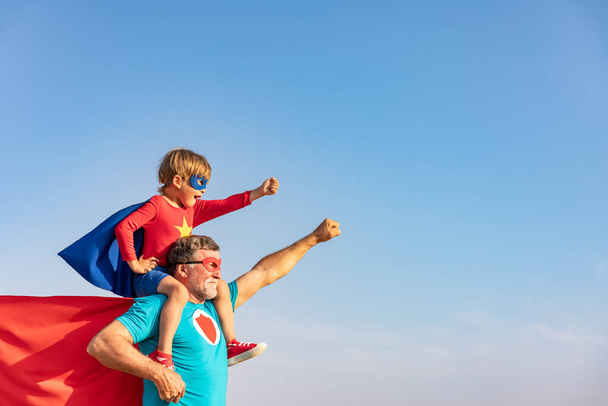 Superhero senior man and child playing outdoor. Super hero grandfather and boy having fun together against blue summer sky background. Family holiday concept. Happy Father's day - Foto, Bild