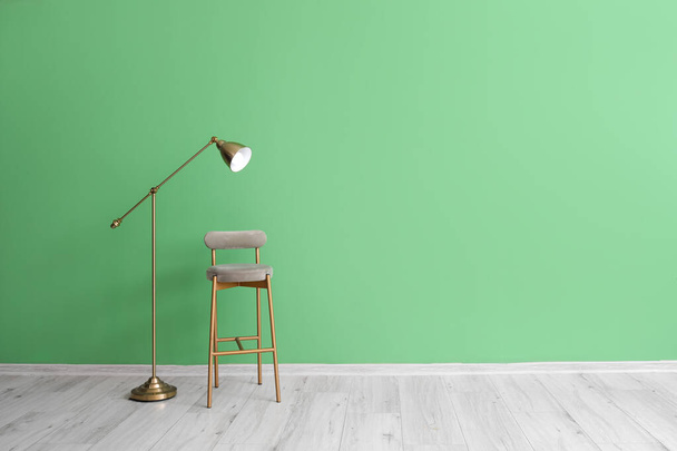 Stijlvolle stoel en standaard lamp nabij groene muur - Foto, afbeelding