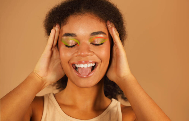 Çekici Afro-Amerikan kadınının güzel moda portresi, şık neon makyajlı güzel bir cazibe modeli, bej renkli stüdyo arka planında izole edilmiş parlak bir gülümsemesi var. - Fotoğraf, Görsel