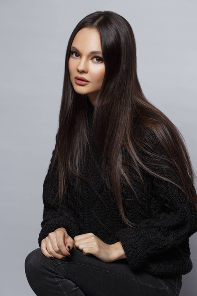 Stylish portrait of a beautiful brunette girl in a black sweater isolated on a gray background. - Foto, imagen