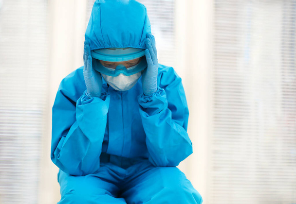Fatigué femme médecin en équipement de protection individuelle EPI se sentant déprimé après un changement stressant difficile pendant la pandémie Covid-19, assis sur le sol à l'hôpital. Travailleurs de la santé dépassés - Photo, image