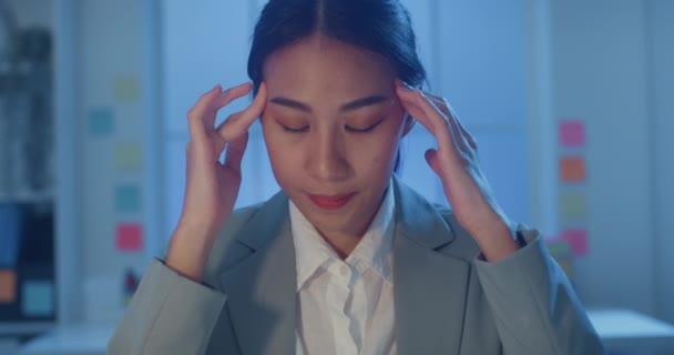 Young Asia businesswoman sit with laptop and tablet on desk rubbing eye feel pain and tired from overwork in office at night. Female suffer of office syndrome long work, Mental Health workplace. - Footage, Video
