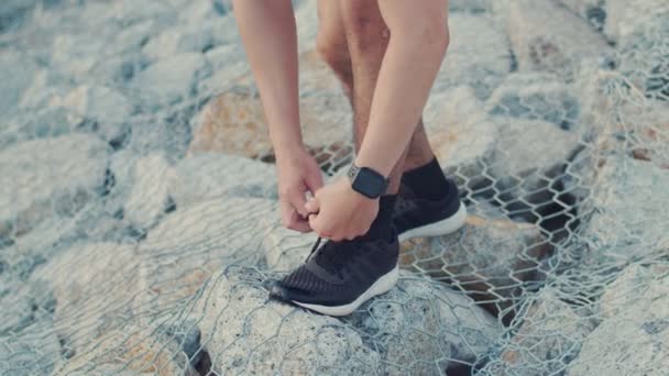 Aziatische man sportieve strikken joggen schoenen voor te bereiden klaar voor het lopen buiten aan de kust. Knappe man werken oefeningen in de zonsondergang. - Video