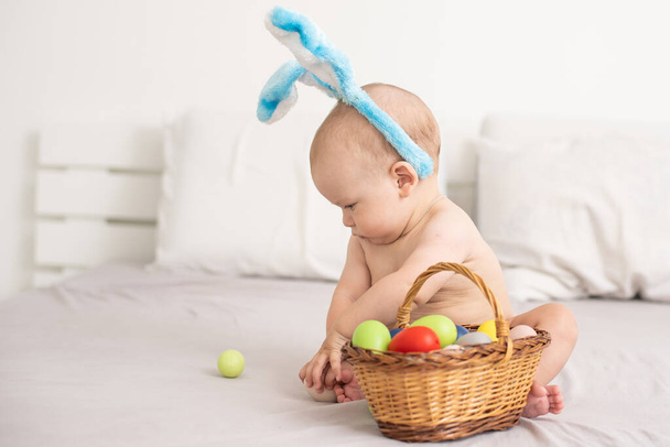 Portrait of a cute baby dressed in Easter bunny ears with a basket full of eggs - Foto, Bild
