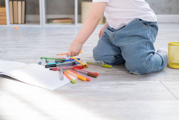krullend kind meisje tekening met gekleurde markers zitten op de vloer in de woonkamer thuis  - Foto, afbeelding