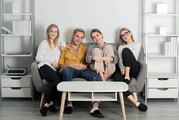 Group of young people sitting on sofa and talking at home. Cheerful young people in casual wear laughing sitting on couch. Positive hipster guys and girls having fun spending time together. - Photo, Image