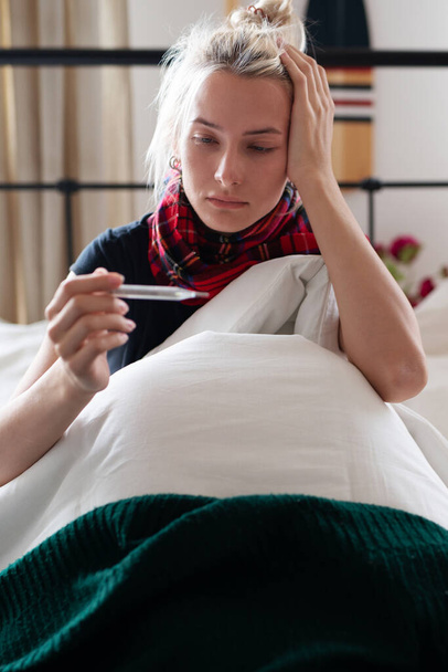Jonge vrouw wordt ziek en neemt haar temperatuur - Foto, afbeelding