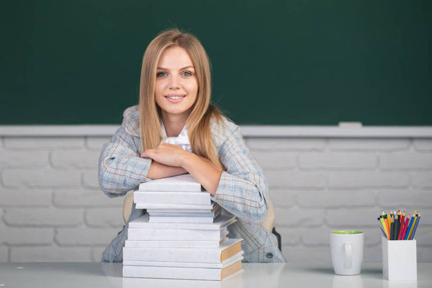 Portrait of a young, confident and attractive female student studying in school classroom. Cute student girl with books on blackboard background with copy space. - 写真・画像