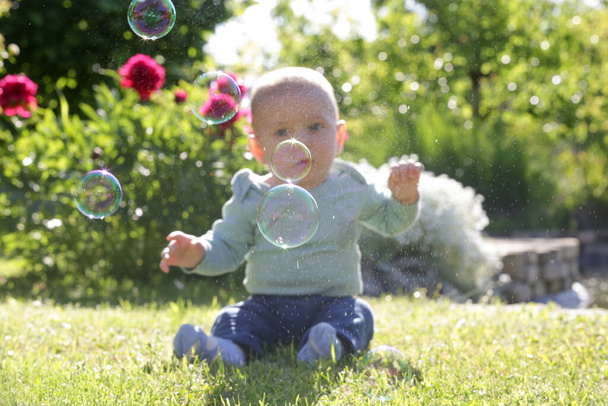 Cute little baby boy playing with soap bubbles in the garden during sunny summer day. Happy childhood concept. - Photo, Image
