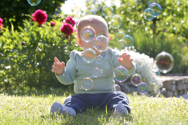 Cute little baby boy playing with soap bubbles in the garden during sunny summer day. Happy childhood concept. - Photo, Image