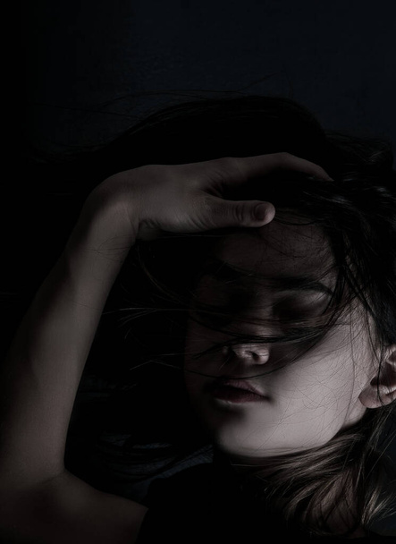 Portrait of a young girl with makeup and long hair in the dark - Photo, Image