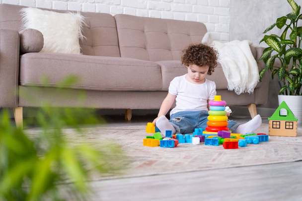 кучерява дівчинка грає з пірамідою і конструктором вдома. розвиток дітей раннього віку
 - Фото, зображення