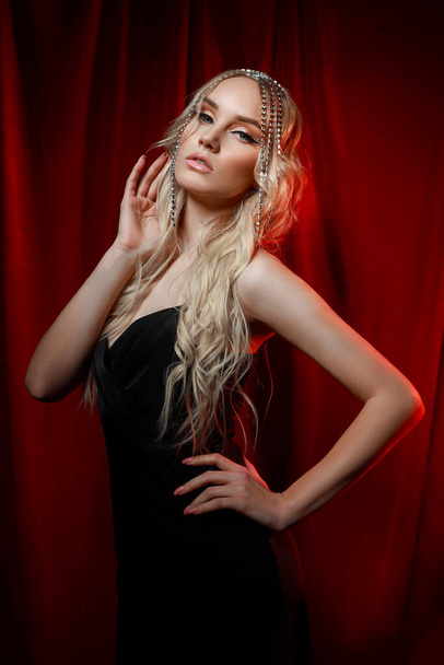 Beautiful blonde woman with long hair on a red velvet background. Hair jewelry on a woman head, modern makeup and arrows on the eyes - Foto, afbeelding