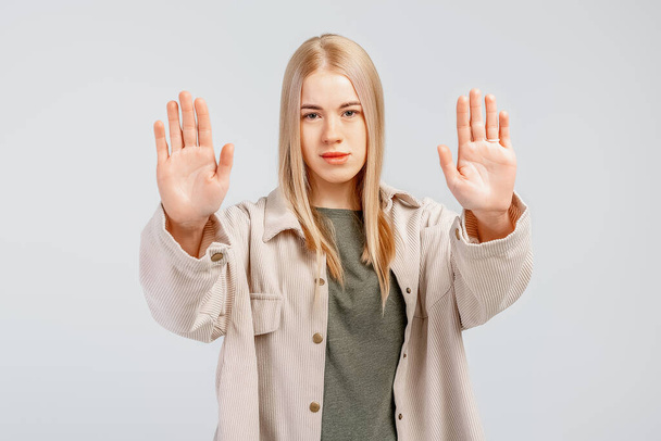 Portrait of a serious girl showing stop sign with palms, stretch out arms, permission denied, prohibit gesture, saying no, rejecting or blocking something, gray background - Foto, Imagem