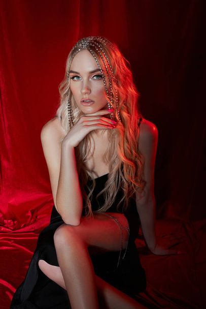 Beautiful blonde woman with long hair on a red velvet background. Hair jewelry on a woman head, modern makeup and arrows on the eyes - Zdjęcie, obraz